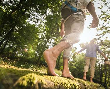 Nackte Füße laufen über einen Baumstamm mit Moos
