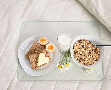 Müsli, Eier und Brot auf einer Platte im Bett