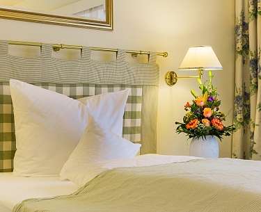 Einzelzimmer mit grün gelb kariertem Bett und Blumenstrauß