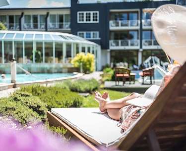 Eine Dame entspannt auf einem Liegestuhl im Außenbereich eines Wellnesshotels 