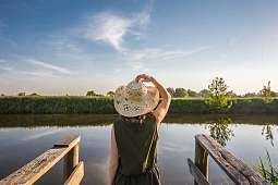 Frau mit Hut von hinten blickt auf einen See