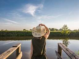 Frau mit Hut von hinten blickt auf einen See