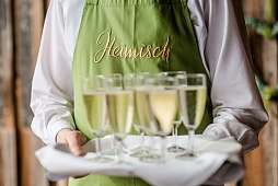 Blick auf Servierteller mit Sektgläsern und grüner Schürze