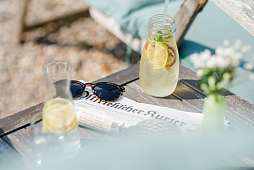 Blick auf einen Tisch mit Sonnenbrille, Zeitung und sommerlicher Limonade