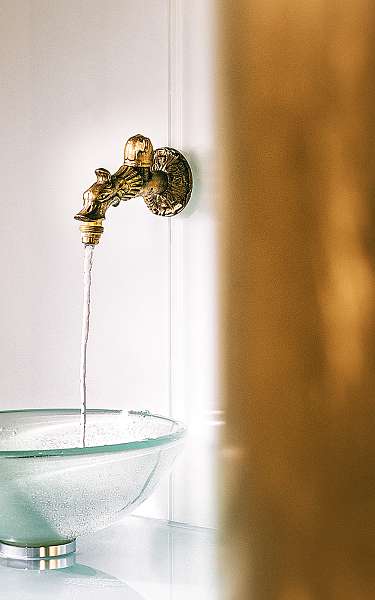 Aus einem goldenen Wasserhahn läuft Wasser in eine Glasschüssel 