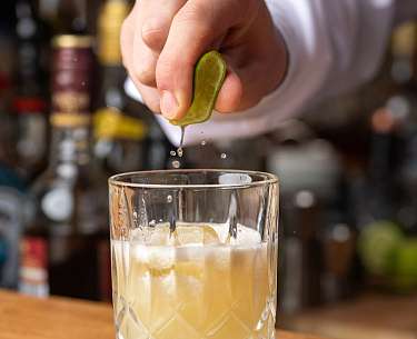 Eine Limette wird über einem Cocktail ausgepresst